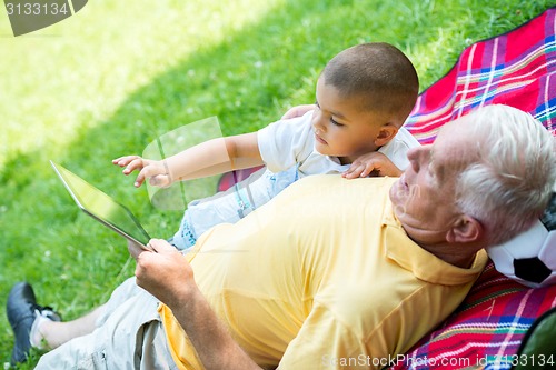 Image of grandfather and child in park using tablet