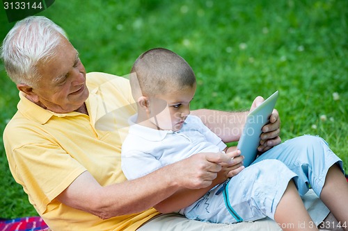 Image of grandfather and child in park using tablet