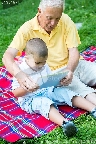 Image of grandfather and child in park using tablet