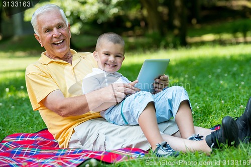 Image of grandfather and child in park using tablet