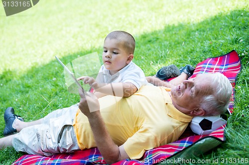 Image of grandfather and child in park using tablet