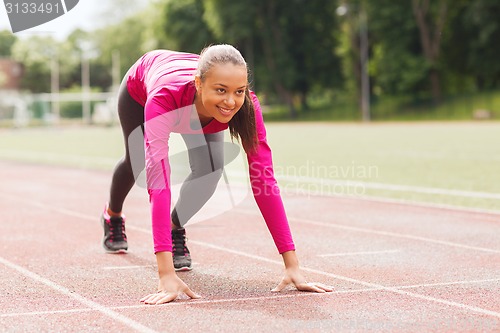 Image of smiling young woman running on track outdoors