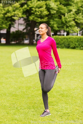 Image of smiling black woman stretching leg outdoors