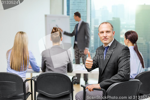 Image of businessman with team showing thumbs up in office