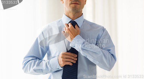 Image of close up of man in shirt adjusting tie on neck