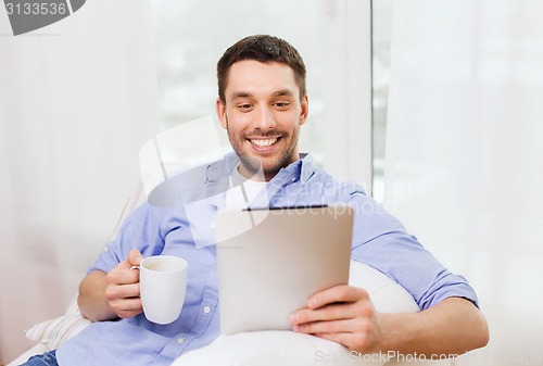 Image of smiling man with tablet pc and cup at home