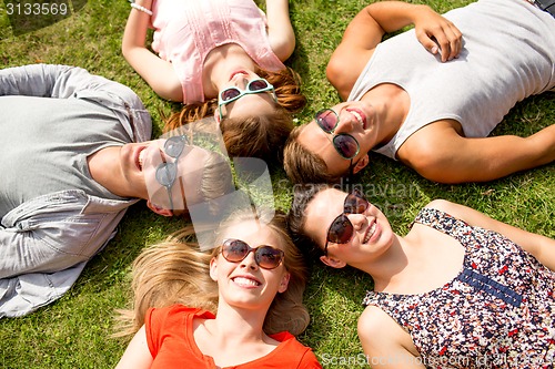 Image of group of smiling friends lying on grass outdoors