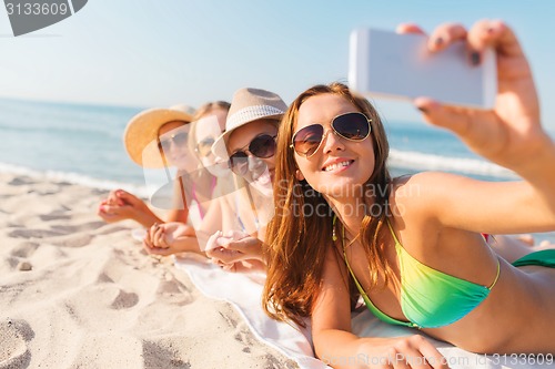 Image of group of smiling women with smartphone on beach