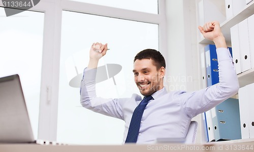 Image of happy businessman with laptop cheering in office