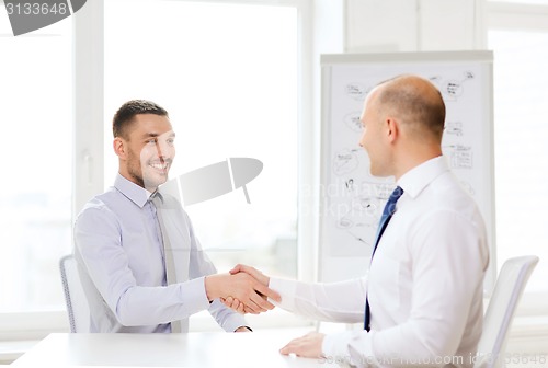 Image of two smiling businessmen shaking hands in office