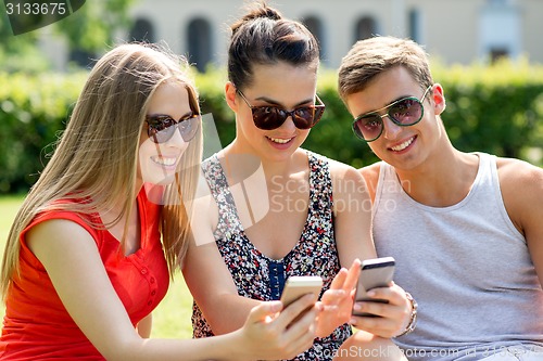 Image of smiling friends with smartphones sitting in park