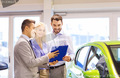 Image of happy couple with car dealer in auto show or salon