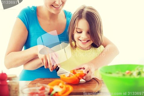 Image of smiling little girl with mother chopping pepper