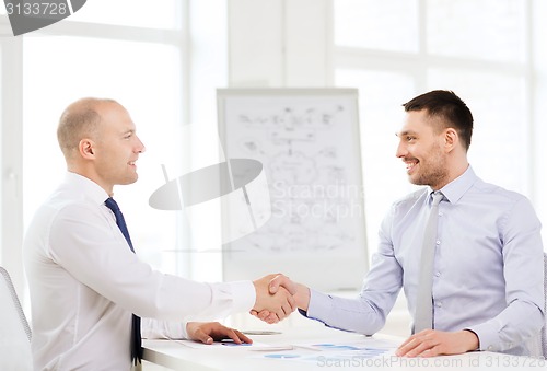 Image of two smiling businessmen shaking hands in office