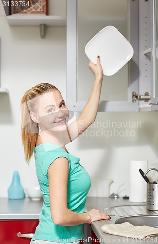 Image of happy woman putting plate to kitchen cabinet