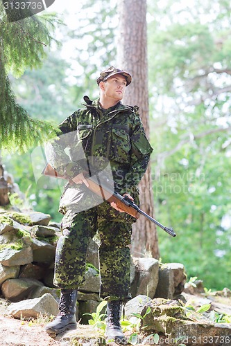 Image of young soldier or hunter with gun in forest