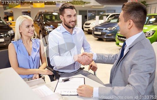 Image of happy couple with car dealer in auto show or salon