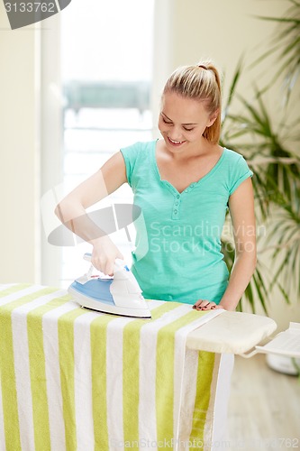 Image of happy woman with iron and ironing board at home