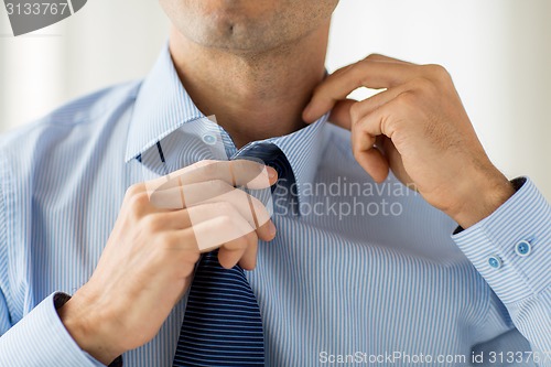 Image of close up of man in shirt adjusting tie on neck