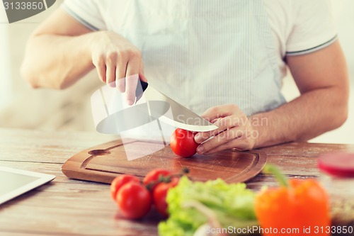 Image of male hand cutting tomato on board with knife