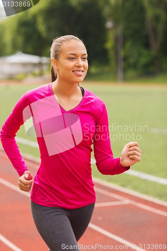 Image of smiling young woman running on track outdoors