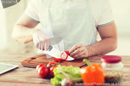 Image of male hand cutting tomato on board with knife