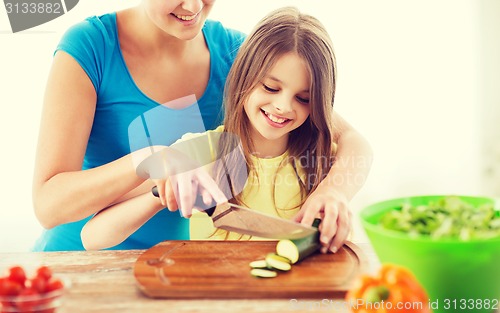 Image of smiling little girl with mother chopping cucumber