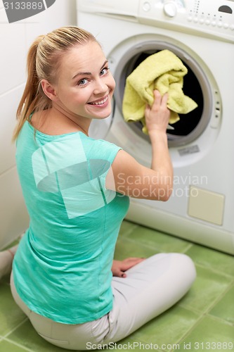 Image of happy woman putting laundry into washer at home