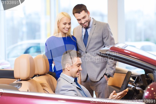 Image of happy couple with car dealer in auto show or salon