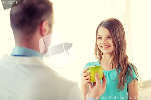 Image of male doctor giving an apple to smiling little girl