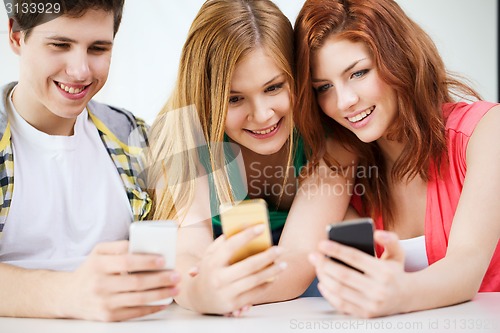 Image of three smiling students with smartphone at school
