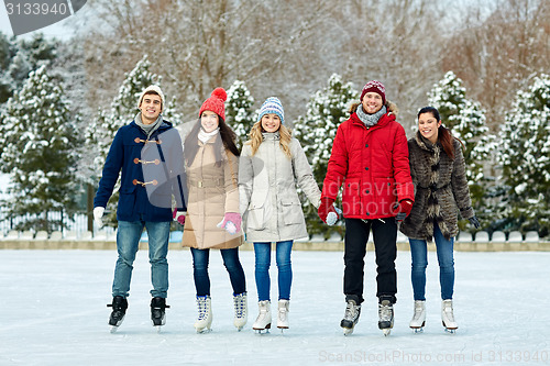 Image of happy friends ice skating on rink outdoors