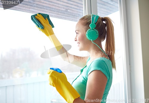 Image of happy woman with headphones cleaning window