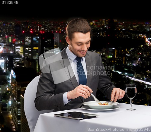 Image of smiling man with tablet pc eating main course