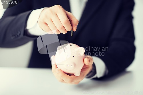 Image of man putting coin into small piggy bank