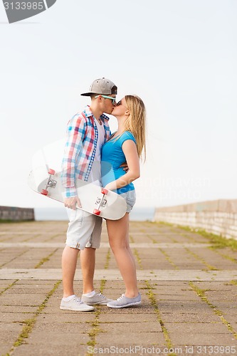 Image of smiling couple with skateboard kissing outdoors