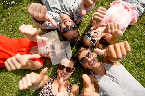 Image of smiling friends showing thumbs up lying on grass