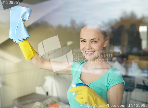 Image of happy woman in gloves cleaning window with rag