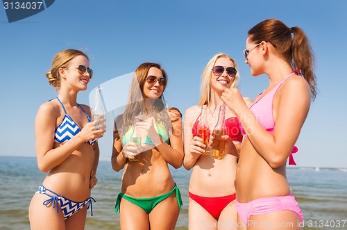 Image of group of smiling young women drinking on beach