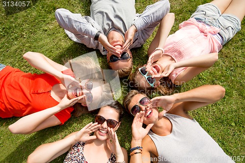 Image of group of smiling friends lying on grass outdoors