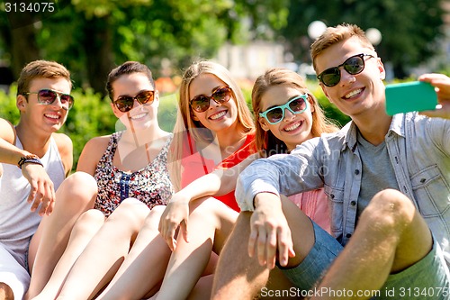 Image of smiling friends with smartphone sitting on grass