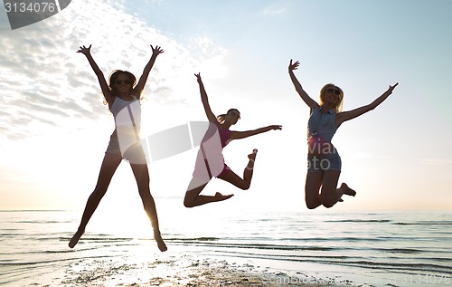 Image of happy female friends dancing and jumping on beach
