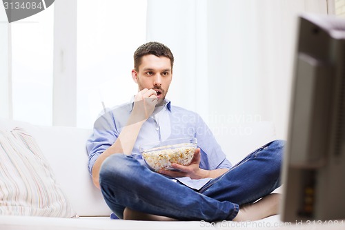 Image of man watching tv and eating popcorn at home