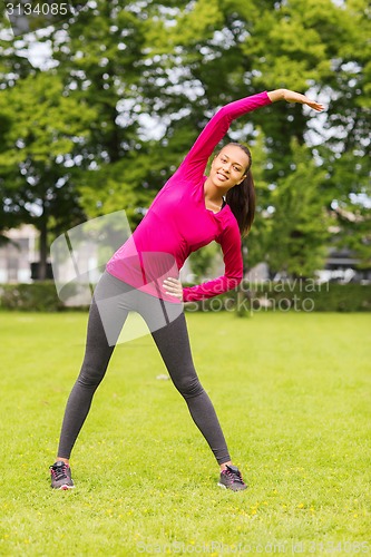 Image of smiling black woman stretching leg outdoors