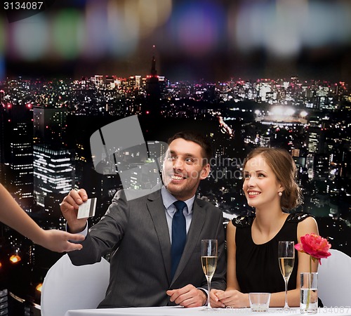 Image of smiling couple paying for dinner with credit card