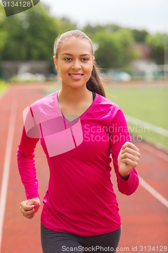 Image of smiling woman running on track outdoors
