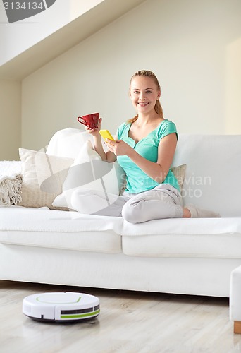 Image of happy woman with smartphone drinking tea at home