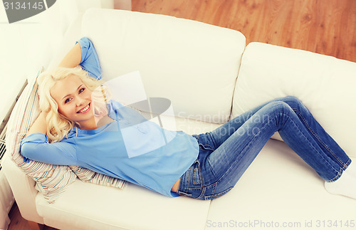 Image of smiling young woman lying on sofa at home