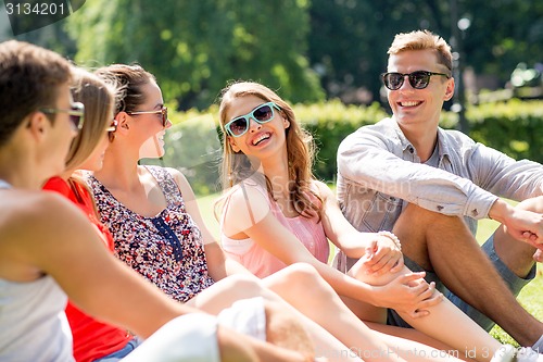 Image of group of smiling friends outdoors sitting in park