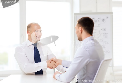 Image of two smiling businessmen shaking hands in office